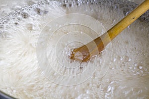 Wooden spoon stirring rapidly boiling liquid close up in cooking