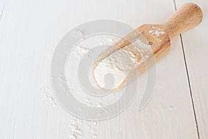 Wooden spoon with wheat flour on white wooden background