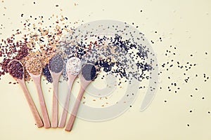 Wooden spoons with assorted seeds isolated on yellow background, chia, linen sesame, healthy food supplements, top view