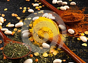 Wooden spoons with multicoloured seasonings on a black textured table. background for kitchen