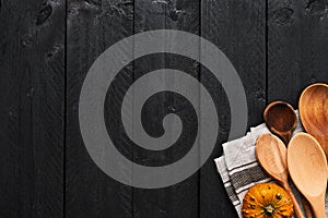 Wooden spoons, pumpkin and dishtowel on black wooden background