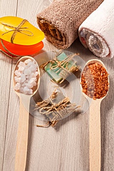 Wooden spoons with white and brown sea salt and handmade soap for bathroom procedures with towels on the background