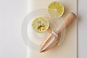 Wooden squeezer and lime cut on half on a table on a white plastic cutting board