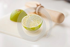 Wooden squeezer and lime cut on half on a table on a white plastic cutting board
