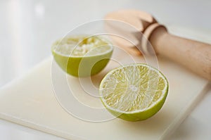 Wooden squeezer and lime cut on half on a table on a white plastic cutting board
