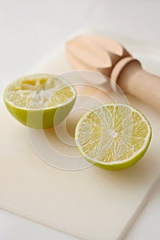 Wooden squeezer and lime cut on half on a table on a white plastic cutting board