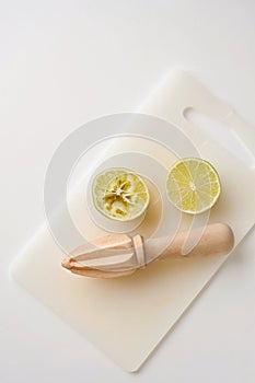 Wooden squeezer and lime cut on half on a table on a white plastic cutting board
