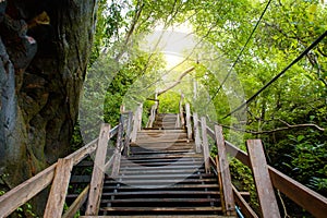 Wooden staircase leads up the mountain towards the sunlight on forest green natural and stone cave It is a beautiful natural