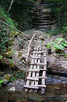 A wooden staircase in the mountains descends to the mountain river from the waterfall