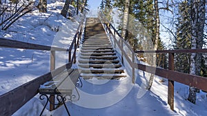 A wooden staircase with a railing rises to a snow-covered hill.