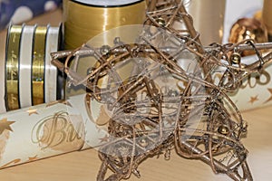 Wooden star in front of materials such as wrapping paper and ribbons to pack and decorate Christmas presents