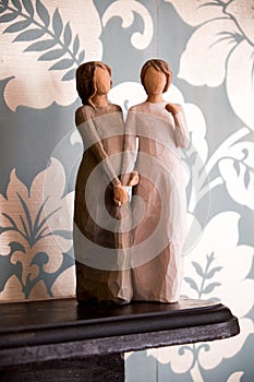 Wooden statue of two women holding hands, statue is on a black