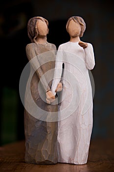 Wooden statue of two women holding hands, statue is on a black m