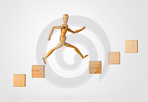 Wooden stick figure jumping from one wooden block on rising steps to the next - achievement, career or objective concept on white photo