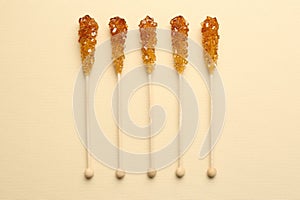 Wooden sticks with sugar crystals on beige background, flat lay. Tasty rock candies