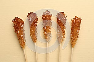 Wooden sticks with sugar crystals on beige background, flat lay. Tasty rock candies