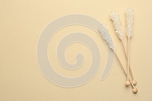 Wooden sticks with sugar crystals and space for text on beige background, flat lay. Tasty rock candies