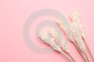 Wooden sticks with sugar crystals and space for text on pink background, flat lay. Tasty rock candies