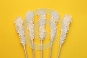 Wooden sticks with sugar crystals on yellow background, flat lay. Tasty rock candies