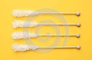 Wooden sticks with sugar crystals on yellow background, flat lay. Tasty rock candies