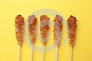 Wooden sticks with sugar crystals on yellow background, flat lay. Tasty rock candies