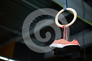 A wooden still ring with women`s pink sneakers or trainers hanging with shoelaces on it on a dark blurred background.