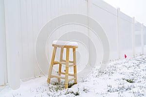 Wooden stool on snow covered ground in winter against white wood fence