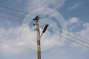 Wooden street lamp post with electric wires against blue sky with white clouds