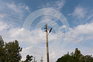 Wooden street lamp post with electric wires against blue sky with white clouds