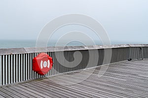 A Wooden structure of the  Pier of Hastings, East Sussex, England with a red lifebelt lifesaver on a day with sea mist in summer