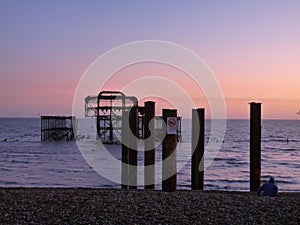 Wooden structure on a rocky beach shoreline illuminated by the warm orange hue of a stunning sunset