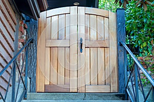 Wooden sturdy gate on front door entrace to house or home with stoop or stairs and black metal hand rails