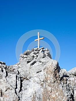 wooden summit cross on a sharp and jagged mountain peak under a blue sky