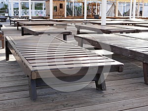 Wooden sun beds stand in the shade on a platform without a single vacationer next to the sea in the early summer morning. photo