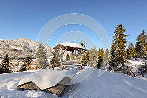 Wooden sunbath lounge bench chair, outdoor picnic table with roof under snow, winter in Tyrol, Europe.