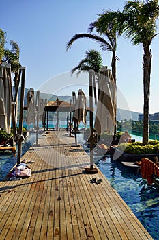 Wooden sunbeds and parasols on wooden deck nearby swimming pool in the evening. The outdoor recreation in luxury hotel.