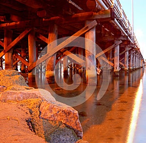 Wooden support of pier bridge over river and rock