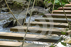 A wooden suspended rope bridge is stretched over a mountain river, selective focus, rocky shores and wild vegetation.Concept: a da