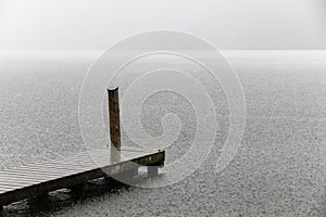 Wooden swimming platform as bridge docking pier deck on an alpine lake during heavy rain with nobody