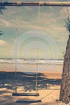 Wooden swing hanging from tree on the beach with seascape view background.