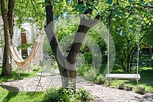 Wooden swing on ropes and hammock under the big tree in the garden.