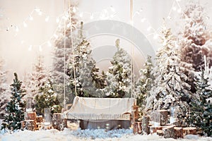 Wooden swing in a snow-covered park or forest with spruce trees and stumps, big candles in glass vases, while snowing