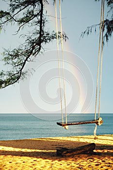 Wooden swings beside the sea with rainbow sky background