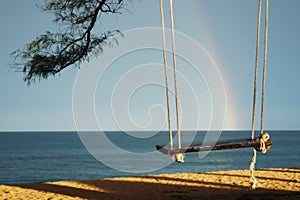 Wooden swings beside the sea with rainbow sky background