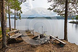 Wooden table and benches in the forest on the lakeside with a fireplace and grill in northern Sweden