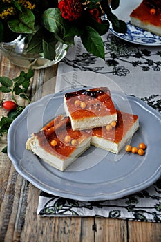 On a wooden table on a blue plate is a curd cake with sea-buckthorn. Decorated with flowers and a branch with hips