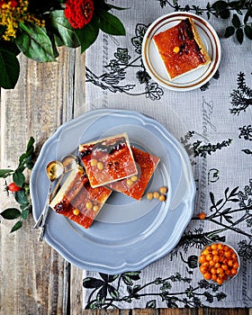 On a wooden table on a blue plate is a curd cake with sea-buckthorn. Decorated with flowers and a branch with hips.