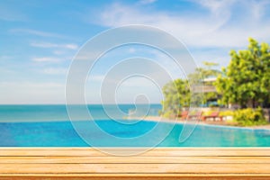 Wooden table with Blurry image of Tropical beautiful seascape view of pool and blue sky in background.