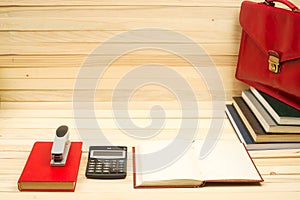 On a wooden table books, documents, calculator, red briefcase.