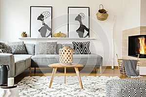 Wooden table on carpet in african living room interior with patterned cushions on grey sofa. Real photo